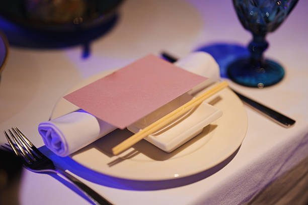 A beautifully arranged table showcases a cream-colored plate with a folded napkin, chopsticks placed neatly, and a small dish. A decorative glass completes the setting.
