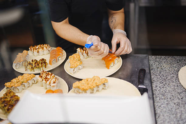 Chef prepares sushi rolls with colorful toppings in a busy kitchen setting