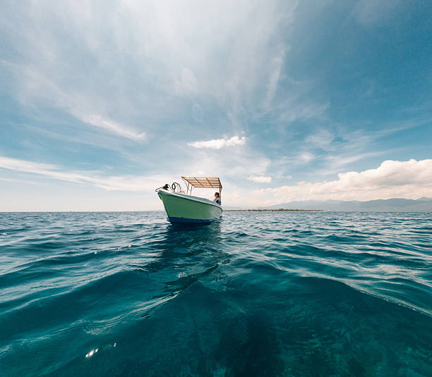 Small boat with a person standing on it, floating on calm turquoise ocean water under a bright blue sky