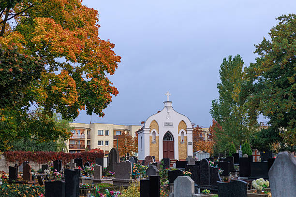 Small white chapel surrounded by colorful autumn trees and gravestones in city cemetery. Concept of memory, heritage, and peaceful atmosphere.