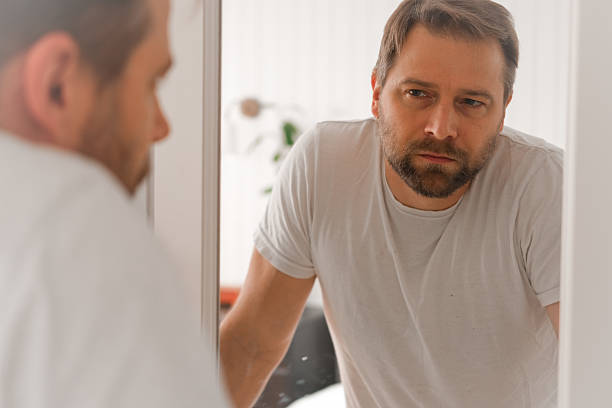 istock Confident handsome bearded man looking himself at the mirror. Pensive guy gazing thoughtfully. Captures introspection, grooming, hair care. Suitable for male health, lifestyle or personal care content 2242552445