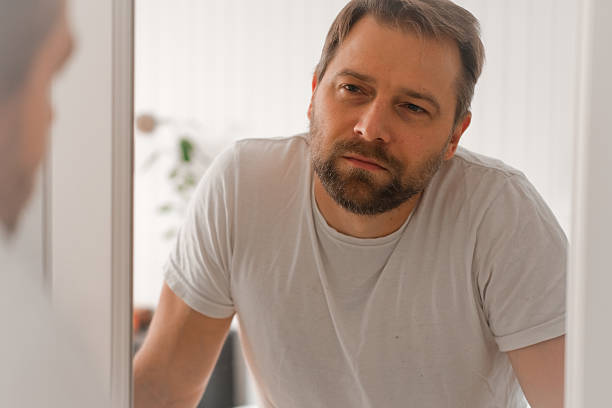istock Confident handsome bearded man looking himself at the mirror. Pensive guy gazing thoughtfully. Captures introspection, grooming, hair care. Suitable for male health, lifestyle or personal care content 2242553126