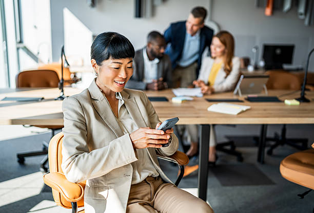 istock Asian businesswoman using smartphone with colleagues in background 2242557442