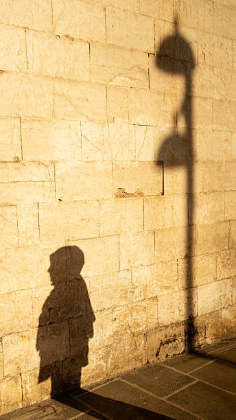 Shadows of a person and lamppost cast on an ancient textured stone wall