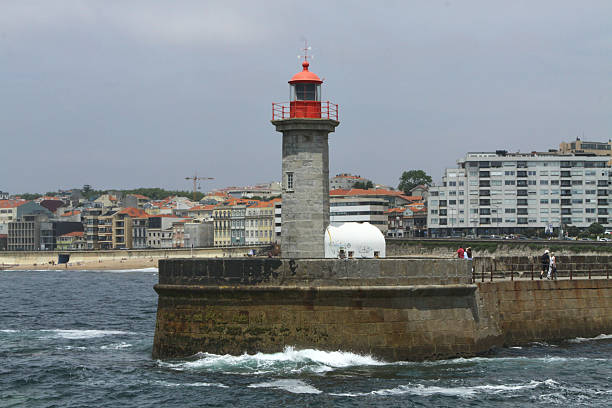 Porto, Portugal - June 10, 2025: Farol de Felgueiras lighthouse is prominently positioned on rocky pier, gazing over Atlantic Ocean, with coastal buildings in background, reflecting maritime history