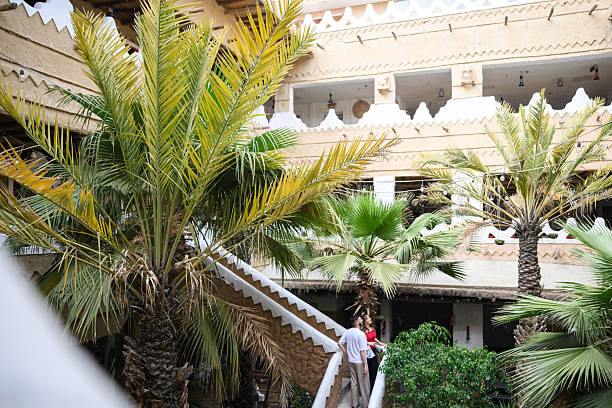 European tourists enjoying traditional architecture of ancient Saudi Arabian culture with brights colours and mud walls with inner oasis courtyard with palm trees