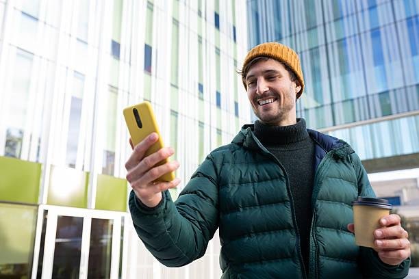 istock Smiling man using smartphone and holding coffee outside office building 2242570097