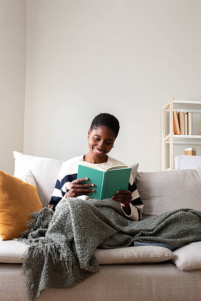 istock Young woman enjoying reading a book on sofa at home 2242570632