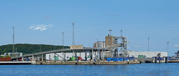 An industrial facility located on the shores of Majorca, featuring storage tanks and facilities for loading or unloading. Surrounded by water, trees, and modern equipment, under a clear blue sky.