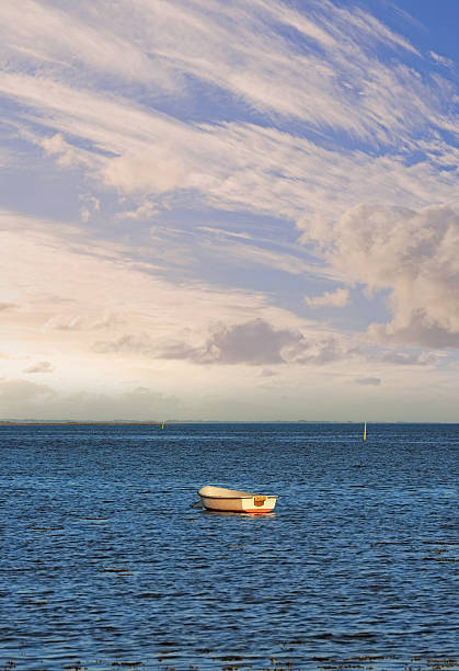 A tranquil scene featuring a single rowboat floating on calm blue waters, set against a backdrop of expansive skies adorned with intricate cloud formations. Perfect for themes of solitude and nature's beauty.