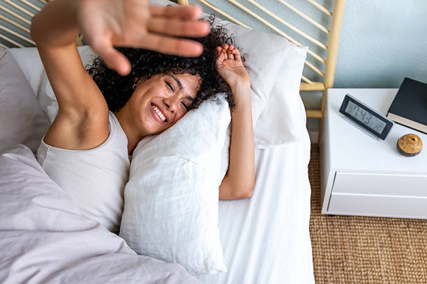 istock Woman waking up happy in bed shielding eyes from morning light 2242573195