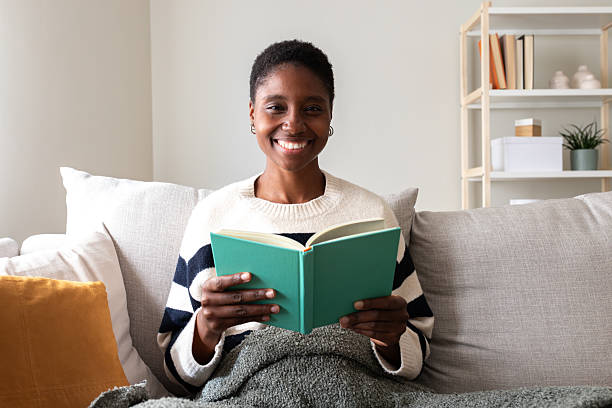 istock Woman smiling while reading book on sofa at home 2242574256