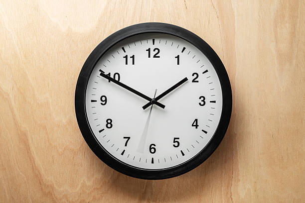istock Analog wall clock with black frame and white dial hanging on a light wooden wall, showing the time at 1:50. A minimalist and classic timepiece symbolizing punctuality, routine, and modern interior decoration. 2242575851