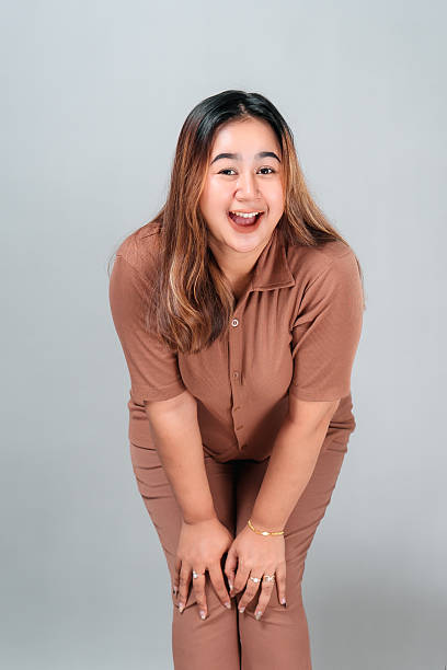 istock Cheerful young Asian woman smiling brightly while bending slightly forward, showing excitement and friendliness. Her joyful facial expression conveys happiness and positive energy. 2242578373