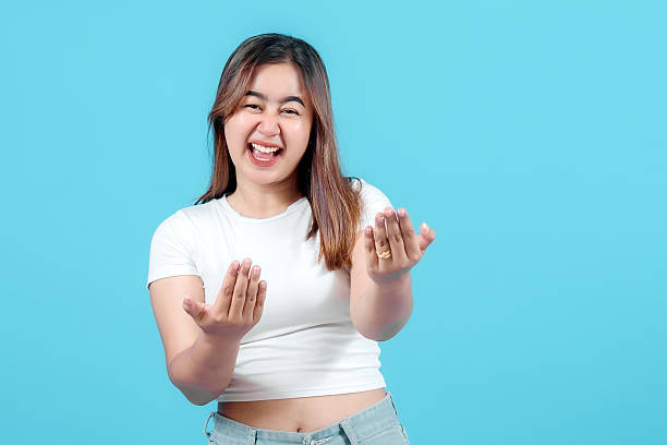istock A joyful young woman laughing and playfully gesturing with her hands, set against a bright blue background, exuding warmth and friendliness. 2242579184