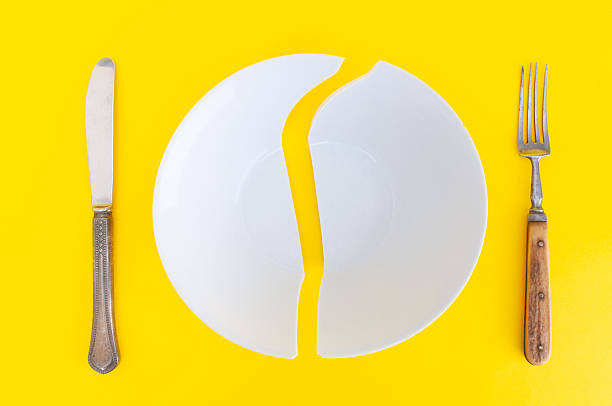 istock Broken plate with antique fork and table-knife  close up on a yellow background 2242579305