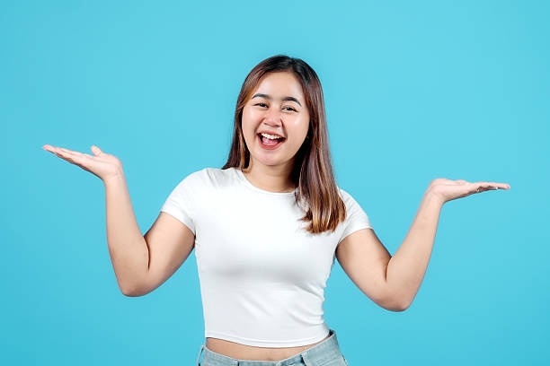 istock Cheerful young woman holding both hands out, presenting two options or comparing products against a blue background. 2242580568