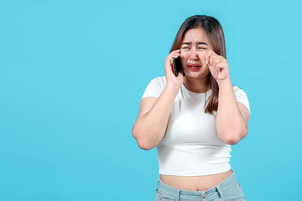 istock A distressed young woman cries while talking on her smartphone, expressing sadness and frustration against a bright blue background. 2242581048