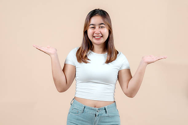 istock A smiling young woman with her hands outstretched, palms up, invitingly presenting something, set against a soft beige background, radiating warmth and friendliness. 2242581421