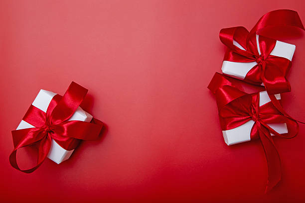 istock White gift boxes with red ribbons on red background. Festive backdrop for banner, advertising or holiday greeting design. 2242582347