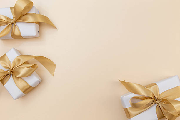 istock Gift boxes with golden satin ribbons on soft beige background. Elegant minimal composition with copy space for text or logo. 2242584398