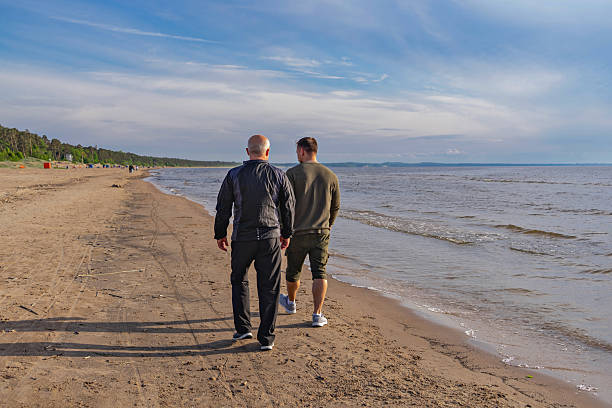 Rear view of father and son strolling along sandy shoreline, quiet conversation and generational bond in soft light