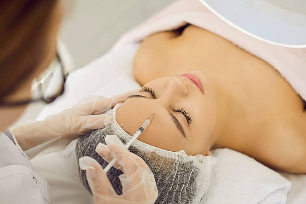 istock Beautician makes patient wrinkle correction with botox in forehead and between eyebrows. 2242590482