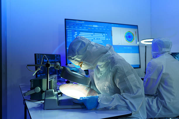 istock Engineers in sterile suits work at a semiconductor manufacturing plant using microscopes in a lab. 2242596141