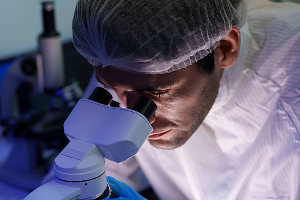 istock Close-up of engineers in sterile suits working in a semiconductor manufacturing plant using a microscope in a laboratory. 2242596155