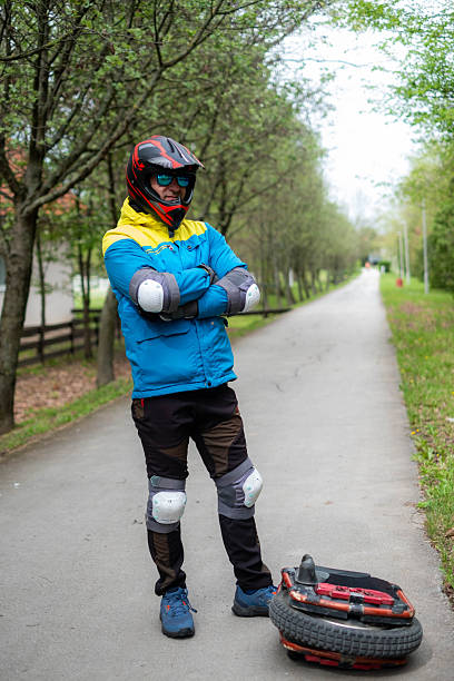 Man wearing a helmet and safety pads standing on a paved path with an electric unicycle