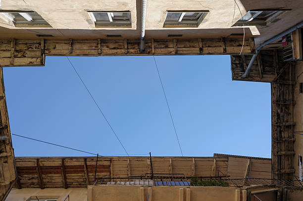 Upward view from a courtyard showing surrounding building walls and a patch of blue sky above, creating an urban geometric composition.