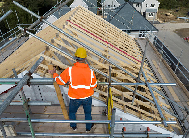Construction worker on building site showing housebuilding,roof trusses, scaffolding and completed houses. Cornwall, UK