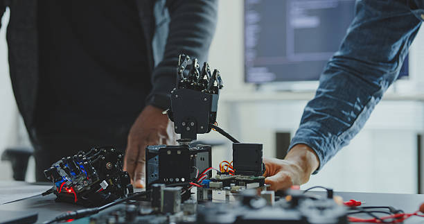 istock Closeup of Black and Hispanic male engineers programmers work together on robot hand prototype, use computer control robotic arm circuit in tech office. Software developer, artificial intelligence. 2242608887