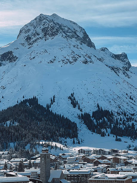 A picturesque winter scene featuring a mountain village and church tower surrounded by snow and forest.