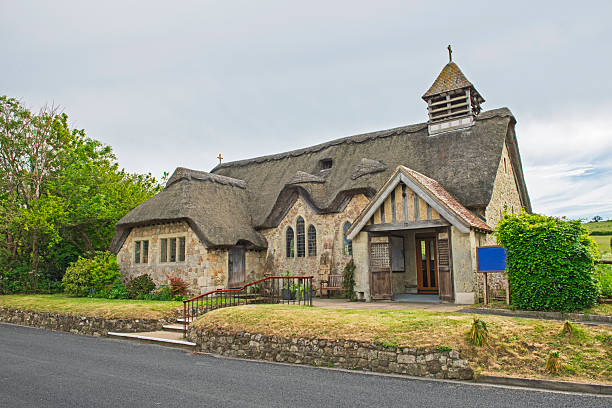 Old tradftional english church building in rural countryside village location setting with thatched roof and field meadows in the background