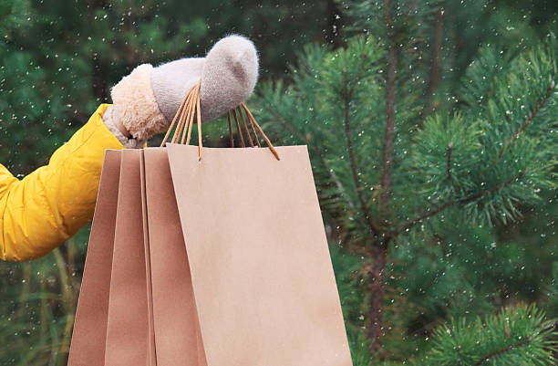 Purchase, holidays, female hand holding showing paper shopping bags, gift against Christmas tree stock photo