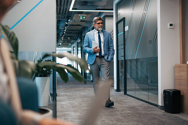 istock Mature businessman walking with tablet in modern office hallway 2242631004