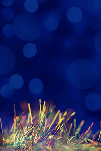 Bright tinsel strands shimmer in a mix of colors, creating a vibrant scene. The background features soft, blurred blue lights that enhance the festive atmosphere. Nice bokeh, space for copy.
