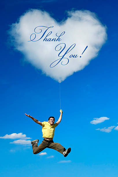A man in a yellow shirt jumps joyfully against a clear blue sky. A heart-shaped cloud floats above him, displaying the words Thank you, expressing gratitude and happiness.