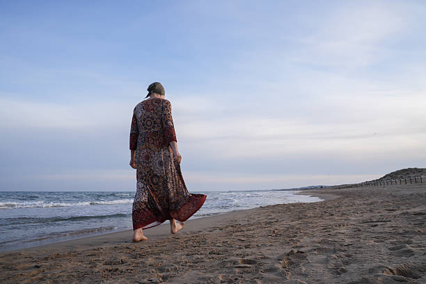 istock Woman with headscarf walking on beach, finding hope 2242635105