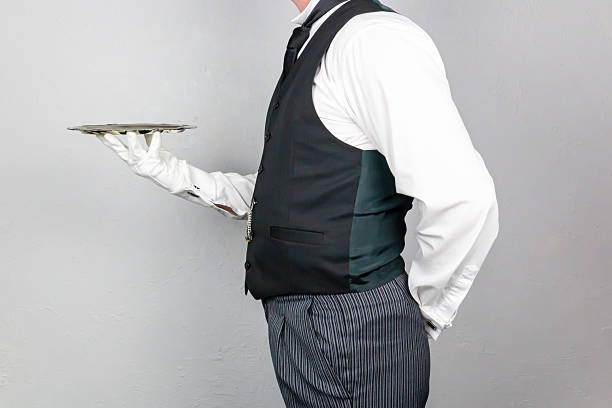 Conceptual image of butler holding bag of money on serving tray, wood paneling behind