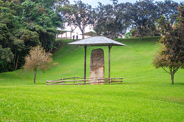 A serene view of a stone statue in San Agustin Archaeological Park, Colombia, surrounded by lush greenery and a protective shelter.