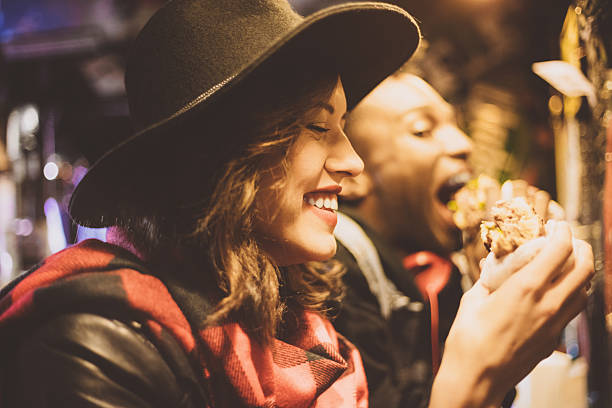 Beautiful young woman wearing black hat eating burger in the pub. Close up of face. Dark tone.