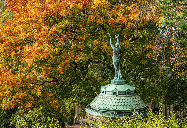 Bronze statue rising amid colorful autumn trees in park