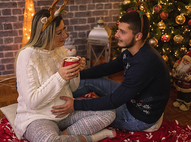 istock Young couple drinking hot chocolate with marshmallows next to the Christmas tree 2242645823