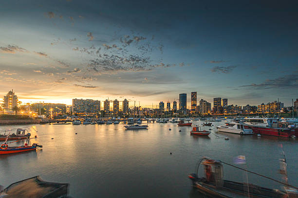 Wide shot skyline of Montevideo at sunset with warm sunshine tones. Shoot at Puerto del Buceo yacht marina. Long exposure for blurred water.