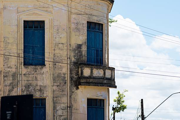 istock Old corner building with tall blue shutters, peeling facade, and balcony under bright sunny sky 2242649614