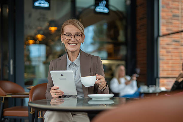 istock Mature businesswoman smiling, drinking coffee, using tablet in cafe 2242650865