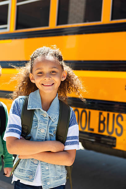 istock Young multiracial girl with backpack smiling by school bus 2242651912