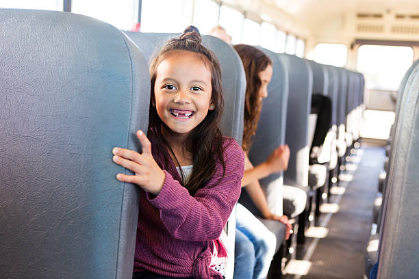 istock Young girl peeks from behind a seat, smiling on a school bus. 2242651923